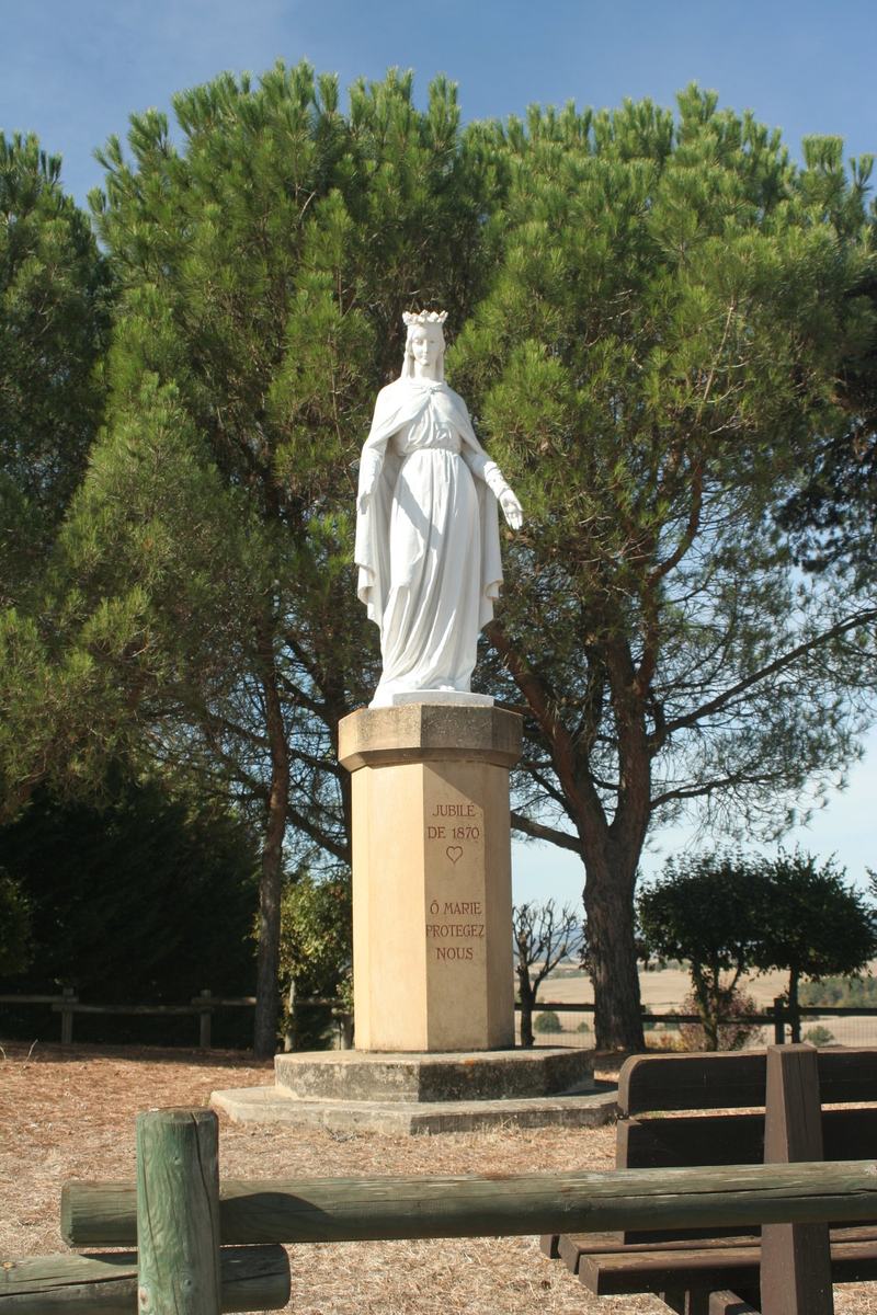 Statue de la Vierge couronnée sur son socle, érigée pour le jubilé de 1870, avec l'inscription « Ô Marie protégez-nous » et vue sur la campagne environnante.