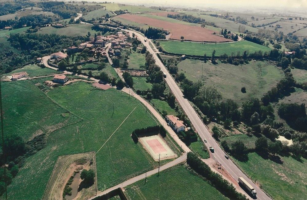 Photographie aérienne couleur du village de Vendranges, avec le terrain de tennis, le cimetière et la route traversant le bourg, septembre 2003.