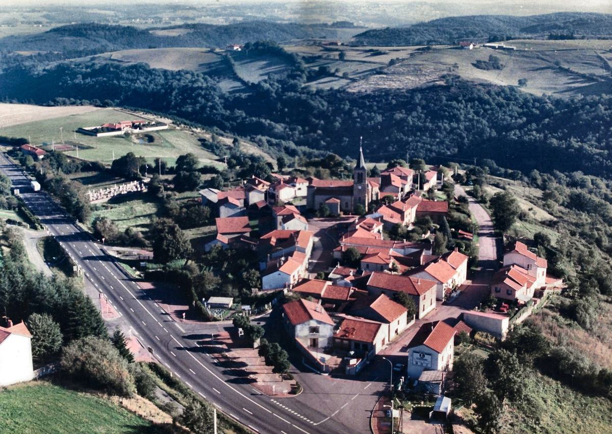 Photographie aérienne couleur du village de Vendranges autour de l'église, avec le cimetière, le terrain de tennis et la route, vers 1995.