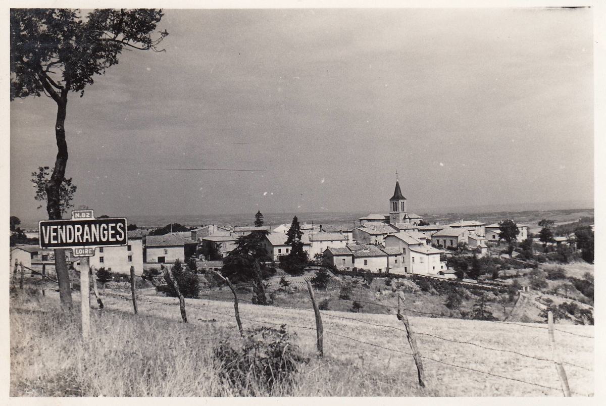Photographie ancienne en noir et blanc : panneau d'entrée « Vendranges, Loire » sur la route N.82, avec vue sur le village et son église, 10 août 1950.