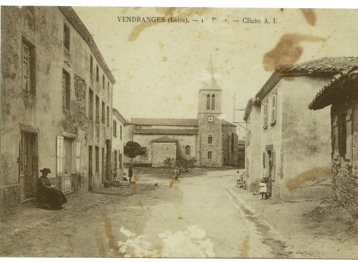Carte postale ancienne en noir et blanc : la place de Vendranges avec des habitants, des enfants et l'église au fond, vers 1915.