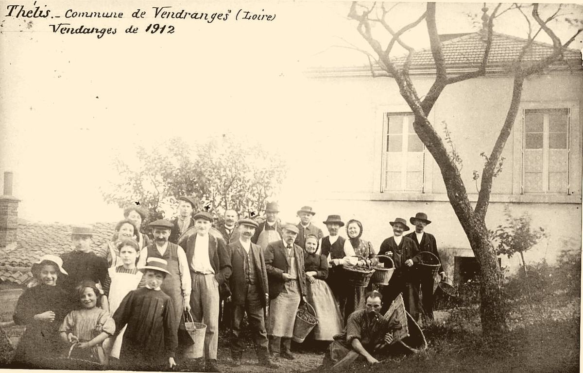 Carte postale ancienne teintée sépia : un groupe de vendangeurs et vendangeuses posant avec seaux et hottes devant une maison, au hameau de Thélis, commune de Vendranges, en 1912.