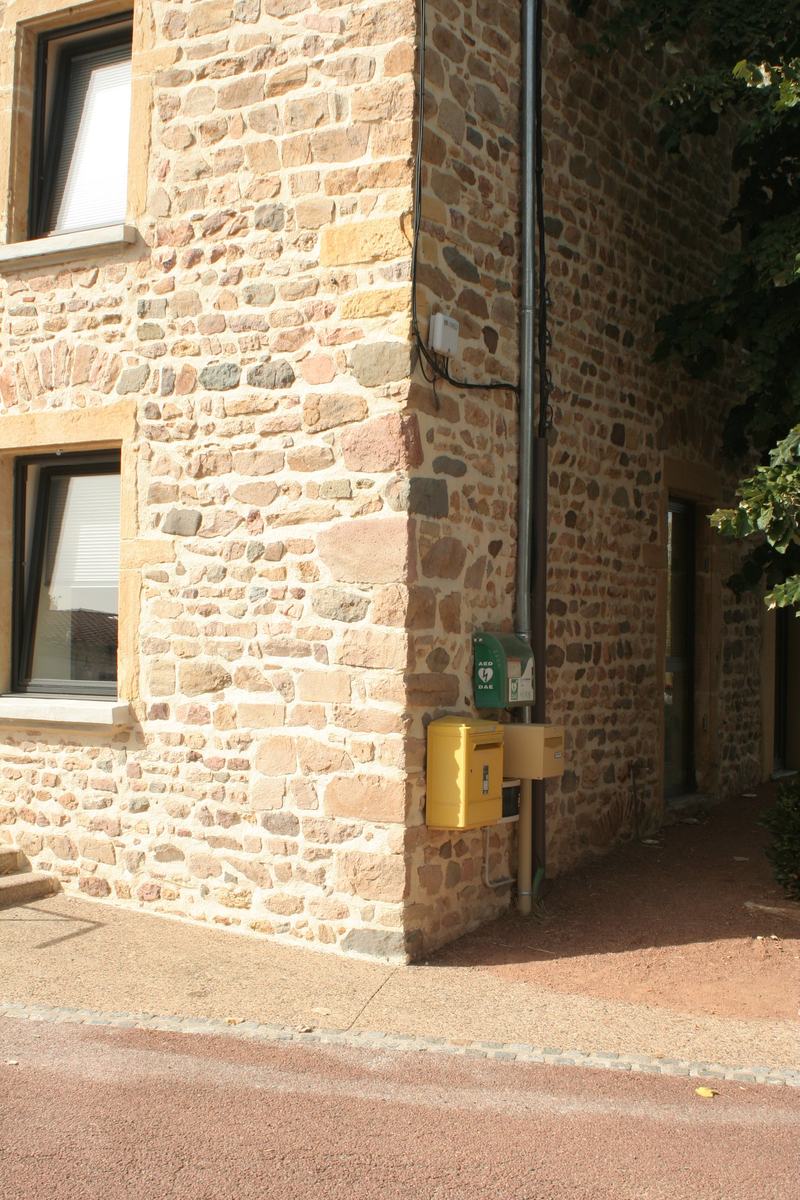 Angle du bâtiment de la mairie de Vendranges, avec le défibrillateur (DAE) et les boîtes aux lettres fixés au mur en pierre.