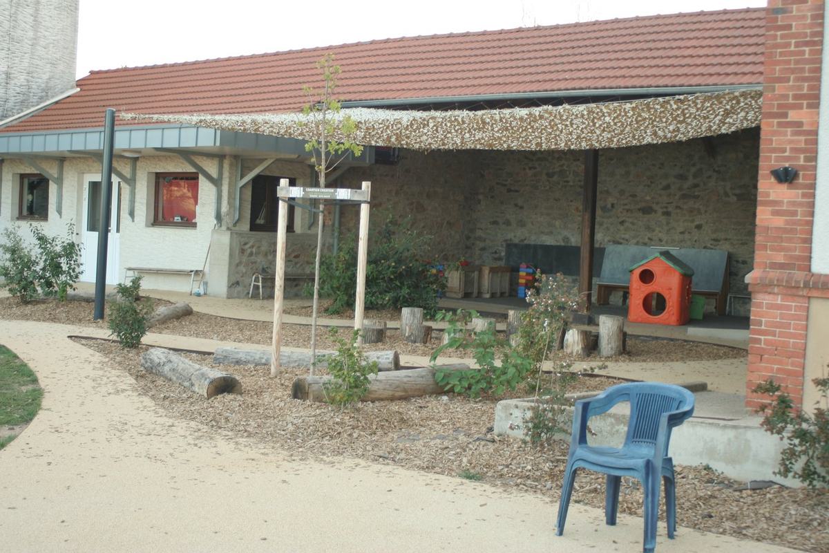 Cour de récréation aménagée de l'école, avec préau et espace ombragé.