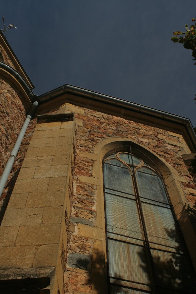 Détail de la façade de l'église Saint-Genest : moellons du pays, contrefort en pierre de taille et fenêtre en arc brisé.